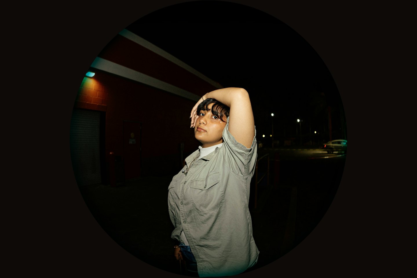 Person posing with hand on head near a brick building.