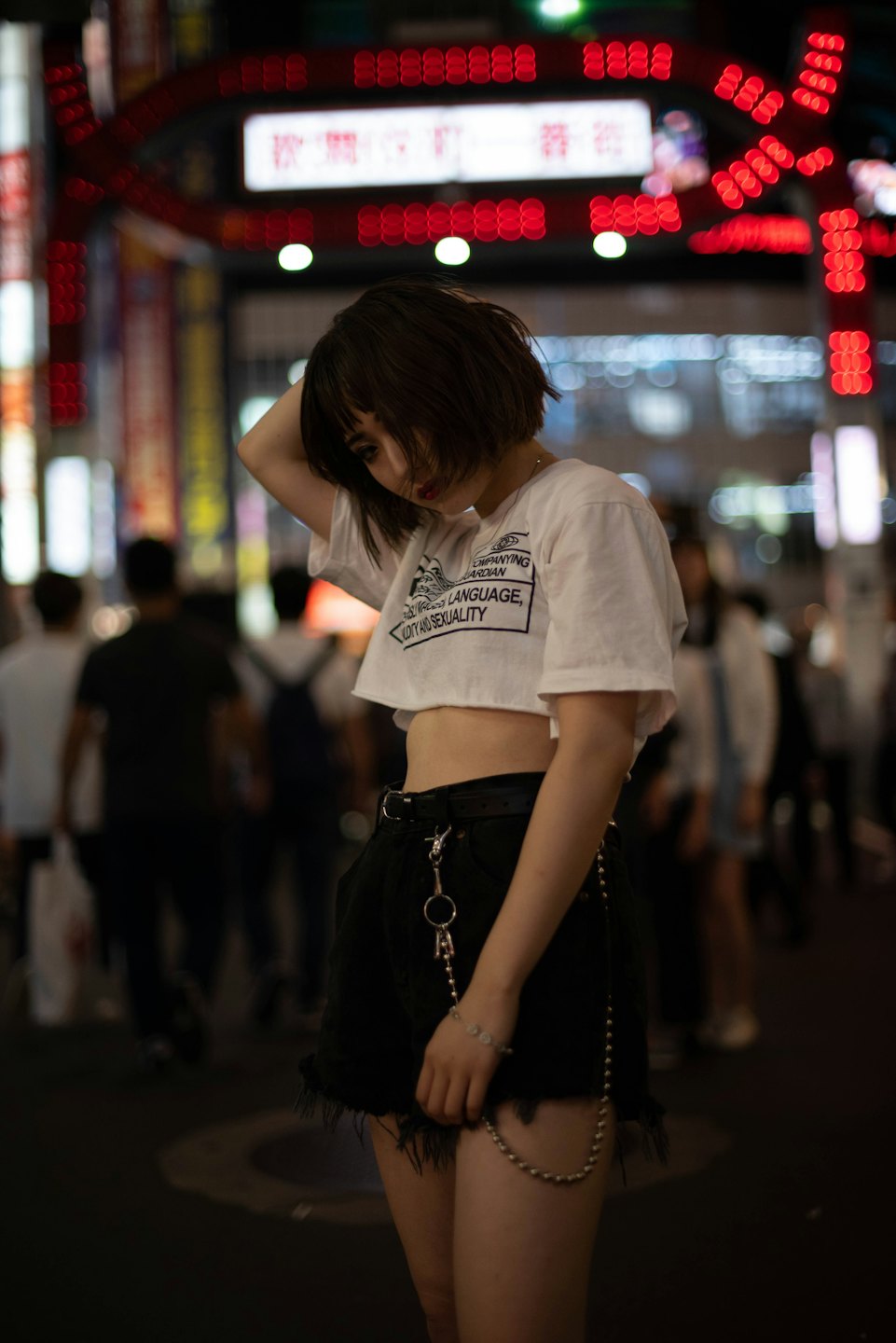 Woman in a t-shirt poses on an urban street at night.