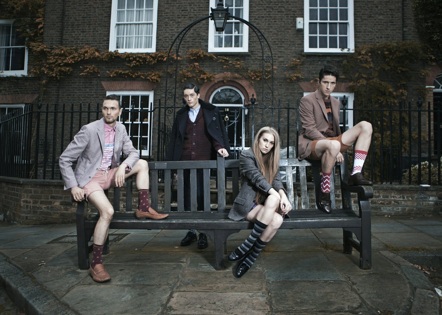 Four young adults on a park bench outside a brick building.