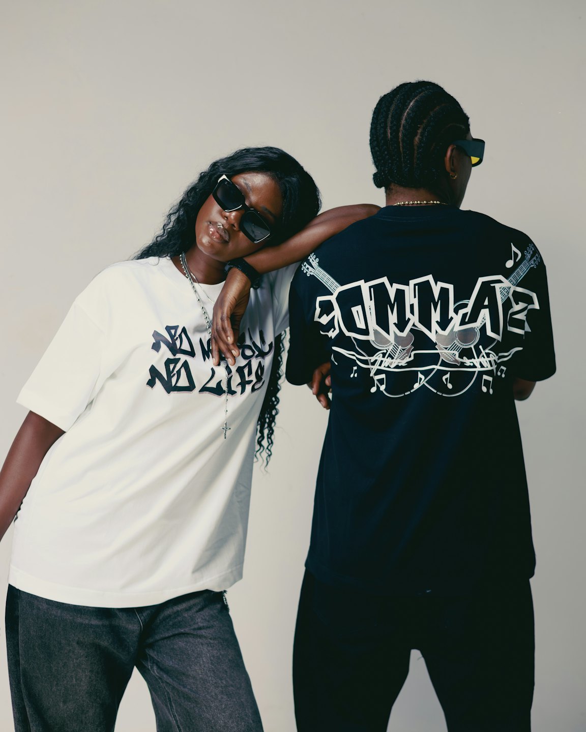 Two people wearing graphic streetwear t-shirts pose against a wall.
