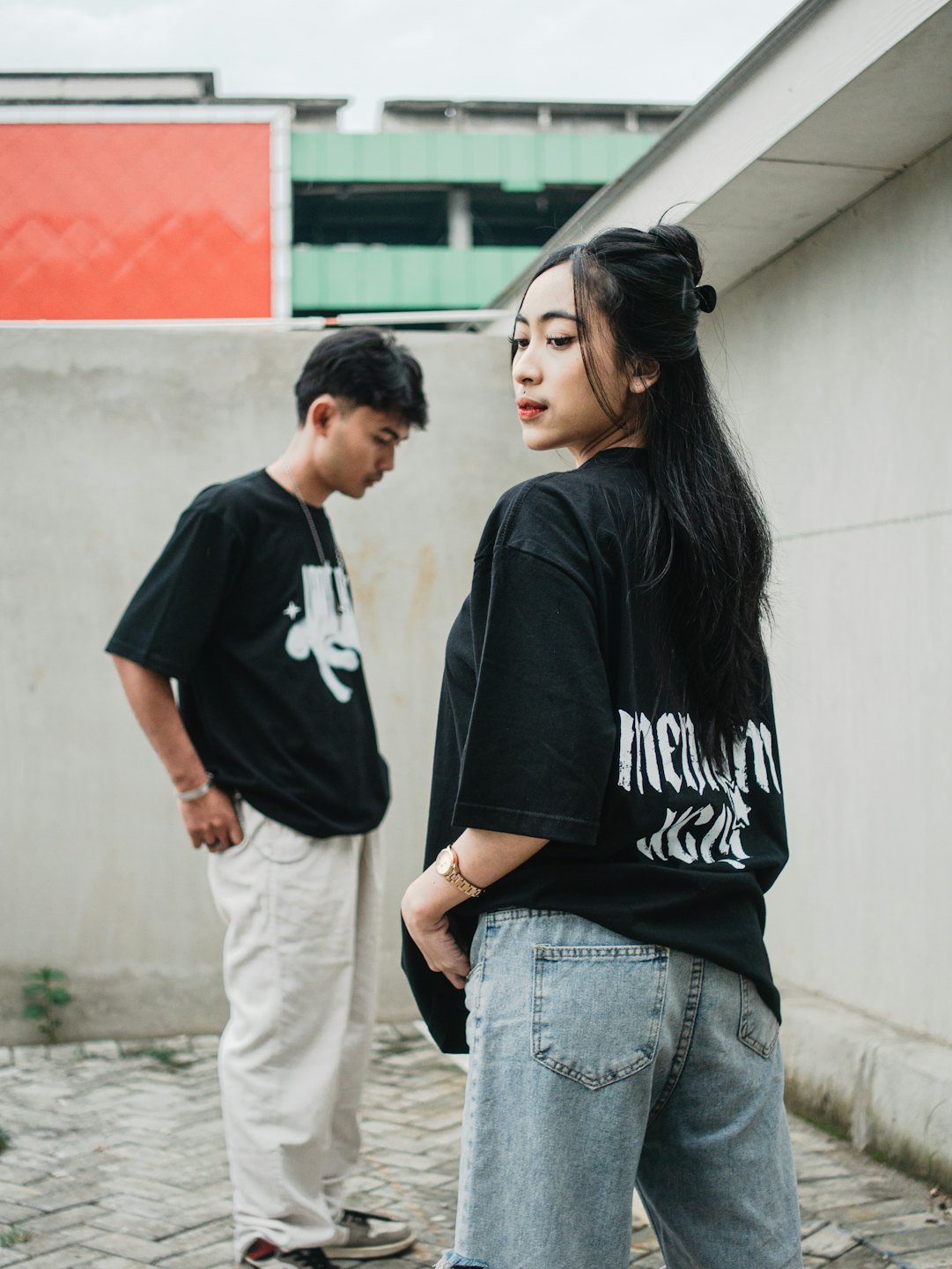 Two people wearing casual streetwear stand by concrete urban walls.