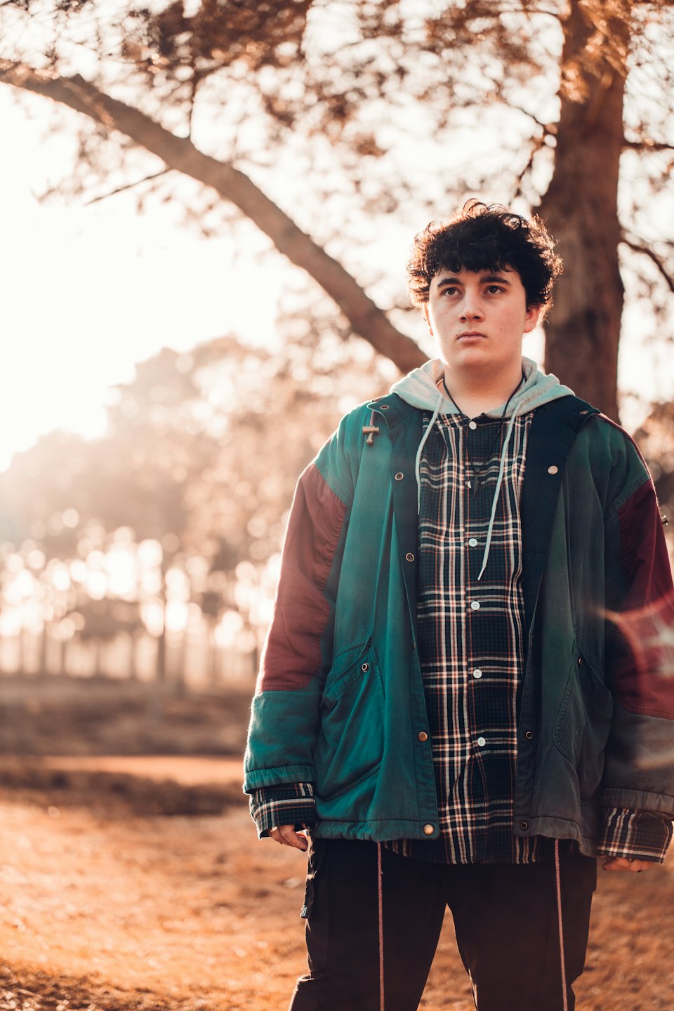 Person in a color-block jacket looks up in park at golden hour.