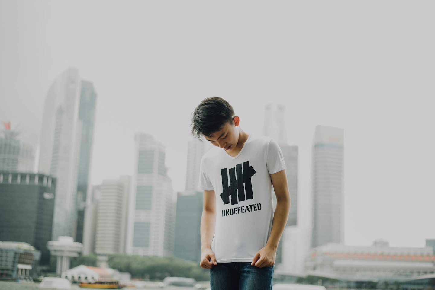 Man in t-shirt and jeans holds shirt standing by skyscrapers.