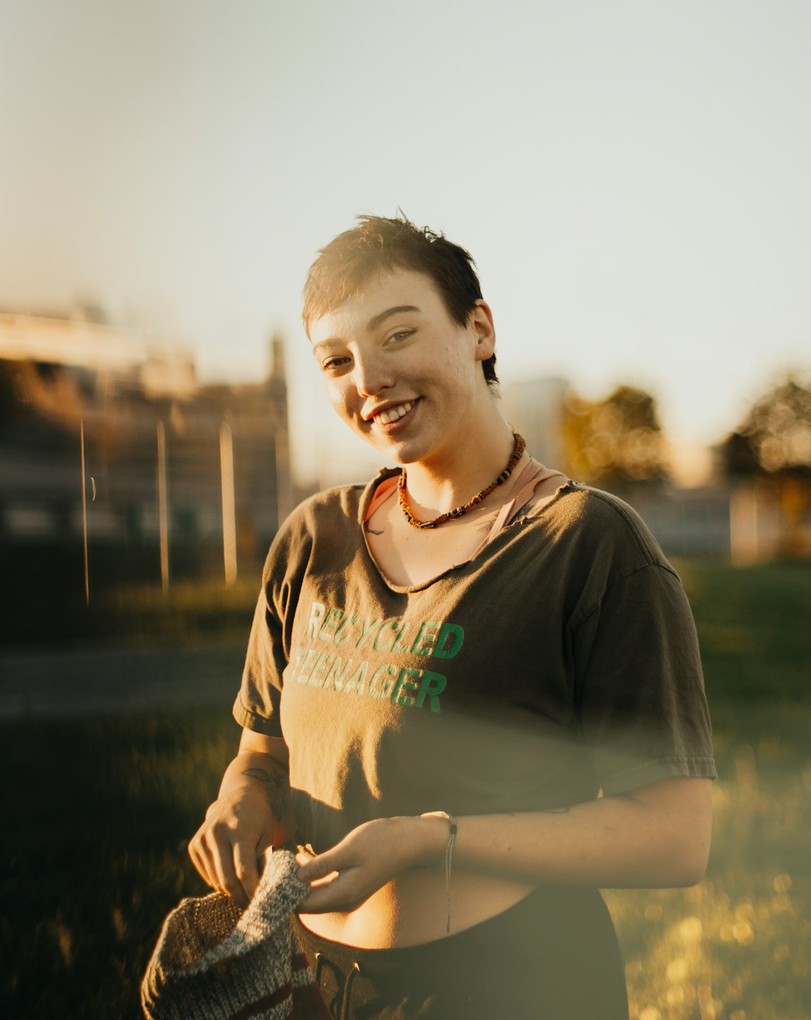A person stands in a park holding a knitted craft.