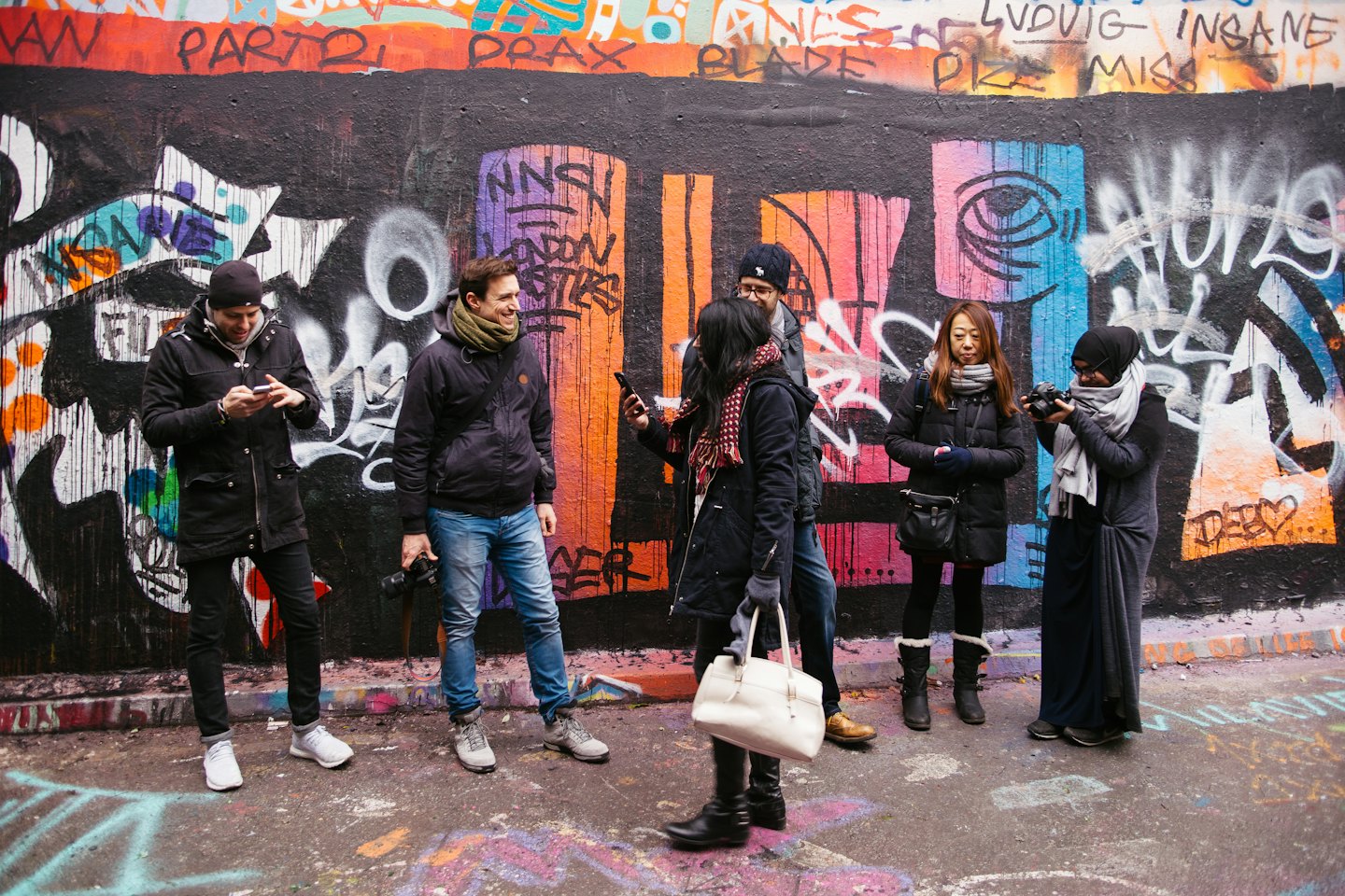 Young adults on a street in front of a graffiti wall.
