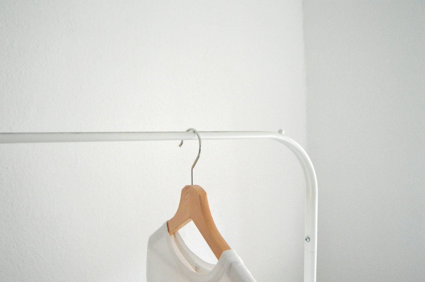 A plain white t-shirt hangs on a wooden hanger.